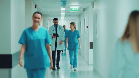 Female Surgeon and Female Doctor Walk Through Hospital Hallway, They Consult Digital Tablet Computer while Talking about Patient's Health.  Shot on RED EPIC-W 8K Helium Cinema Camera.