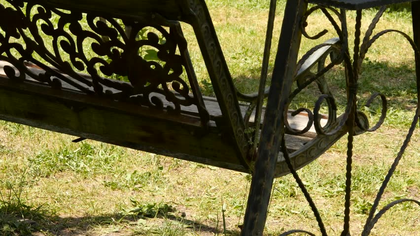 empty forged old swings swaying in a green garden. abandoned garden concept. 4K