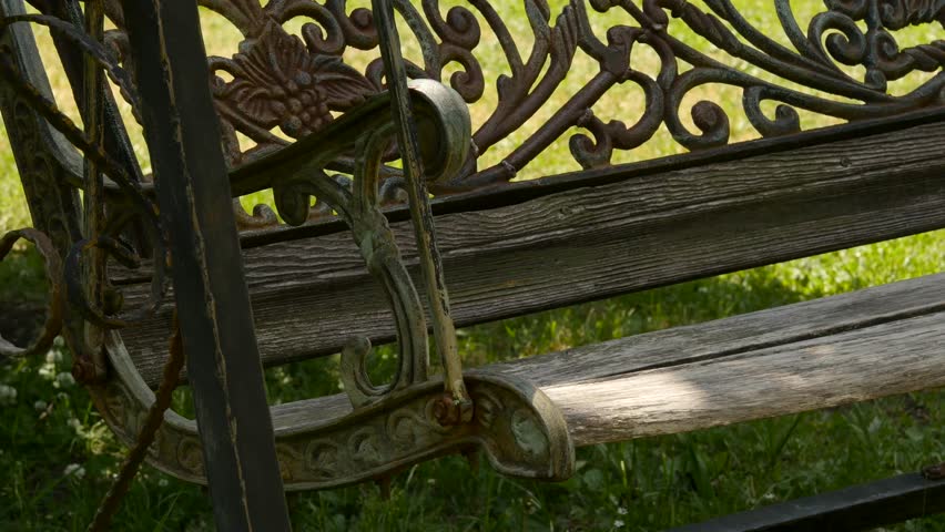 empty forged old swings swaying in a green garden. abandoned garden concept. 4K