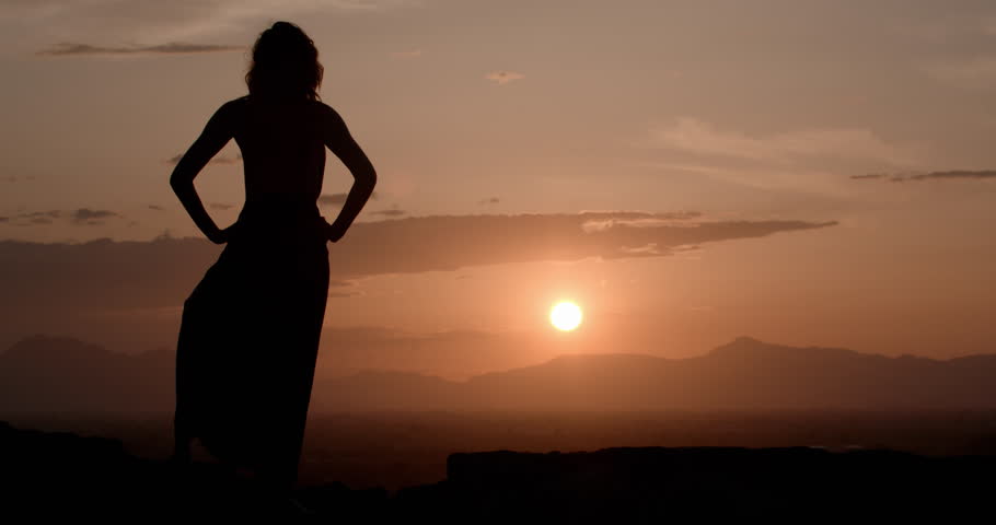 Sexy woman wearing a long black dress models and poses at sunset