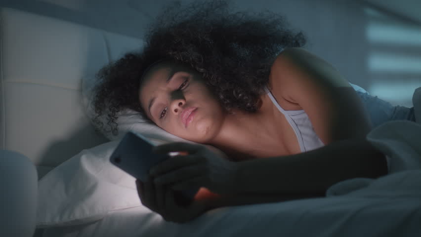 Young latino woman in bed messaging with mobile telephone at home. Tired african american girl in bedroom with cell phone. People using smartphone for texting message before sleeping Royalty-Free Stock Footage #1012621043