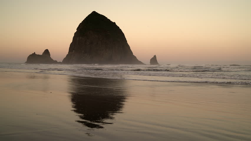 Haystack Rock, Cannon Beach Dawn 4K. UHD. Dawn at Haystack Rock in Cannon Beach, Oregon as the surf washes up onto the beach. United States. Royalty-Free Stock Footage #1012623224