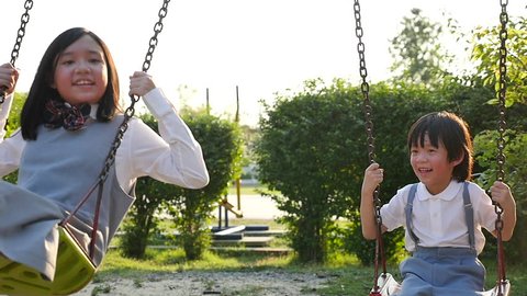 Asian girl and her brother playing swing together in the park slow motion