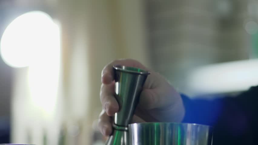 man arms holds jigger and slow pours whiskey into shaker close-up on an unfocused background