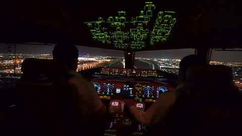 Two pilot were operating the airplane in landing phase. Airplane was touching down on the runway in airport at night, able to see beautiful view of cityscape and lights of runway from inside cockpit.