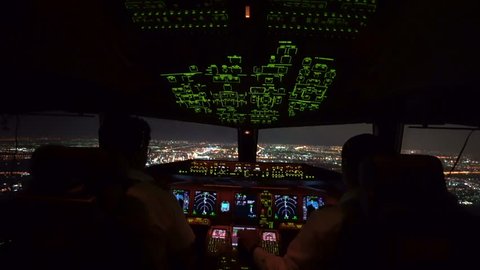 Two pilot were operating the airplane in approach phase toward the runway in airport at night, can see beautiful view of cityscape and lights of runway from inside cockpit.
