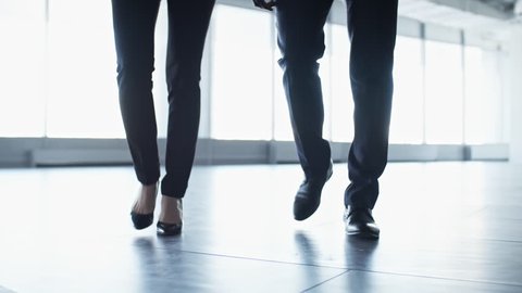 Low-angled shot of legs of businessman and businesswoman walking towards the camera through the lobby in office center