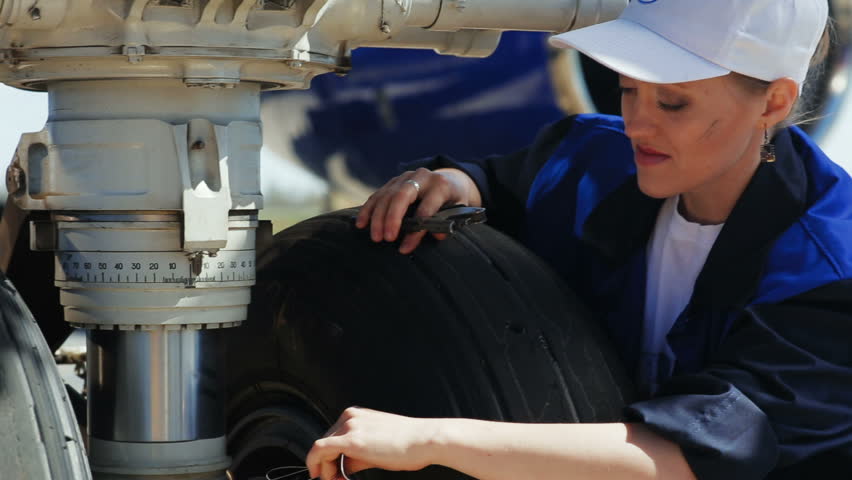 KAZAN, TATARSTAN/RUSSIA - MAY 14 2018: Closeup female airport employee in white cap makes measurements sitting near huge airplane wheel on May 14 in Kazan | Shutterstock HD Video #1012637939