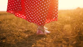 Young girl in red dress walking on meadow with green grass nature slow motion video. girl in the field legs at sunset in a red dress hand close-up on the grass sunlight silhouette. lifestyle woman