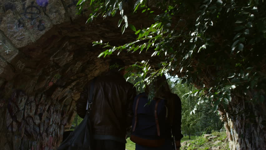 Rear view of two young people with bags walking through stone arch when enjoying walk together