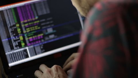Close up of a hacker coding in front of a notebook monitor.