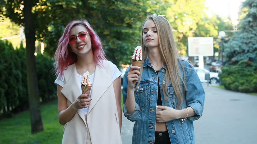 Hipster young adult friends embracing while hanging out in the city. Two young women laughing and walking enjoying carefree vacation lifestyle. Two pretty girlfriends eating ice cream in the city