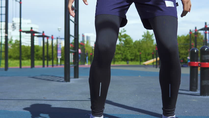The athlete jumps on the bar and jumps back. In the background a street workout park and city landscape.