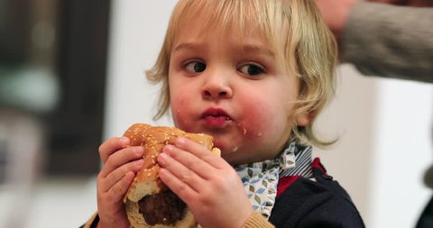 Child eating burger for dinner.  Toddler baby eats hamburger for the first time for supper