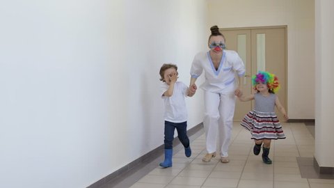 Medical sister in professional uniform with two funny children in the corridor of hospital.