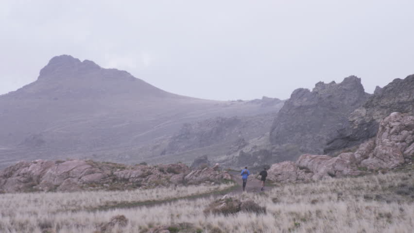 Wide shot of two men running on trail while snow begins to fall