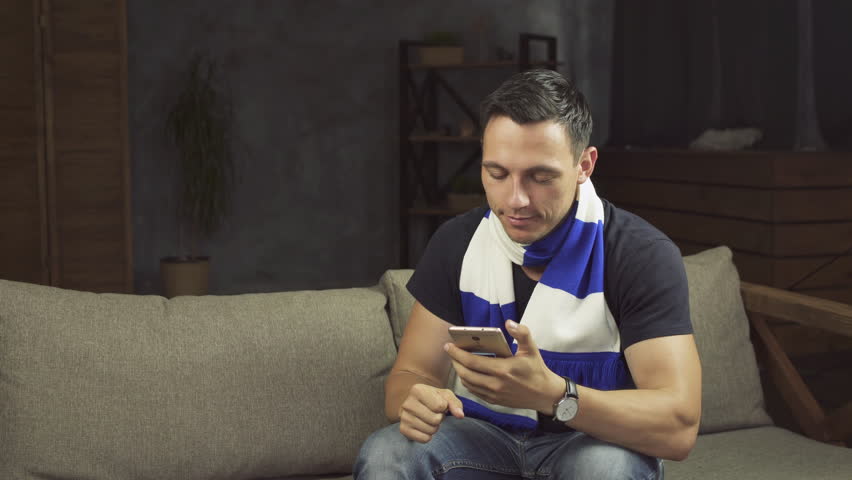 Young euphoric football fan winning a betting and watching a smart phone. Man celebrate win a bet with a gambling mobile app. Soccer bet