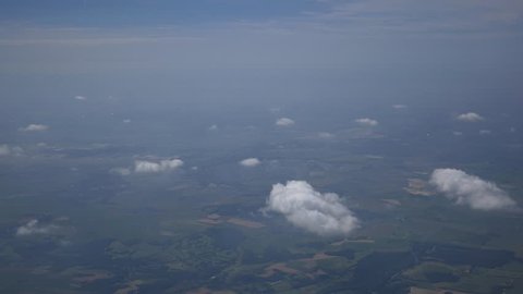 Airplane window view of clouds floating in the clear sky above a green landscape surrounded by water