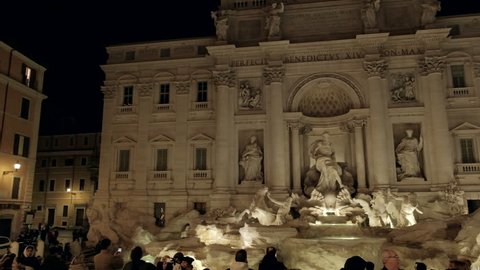 Rome, Italy - February 21, 2018: Camera sweeping panoramic pan left of Trevi Fountain building facade and lighted statues from center rear at night. 4K UHD at 25fps