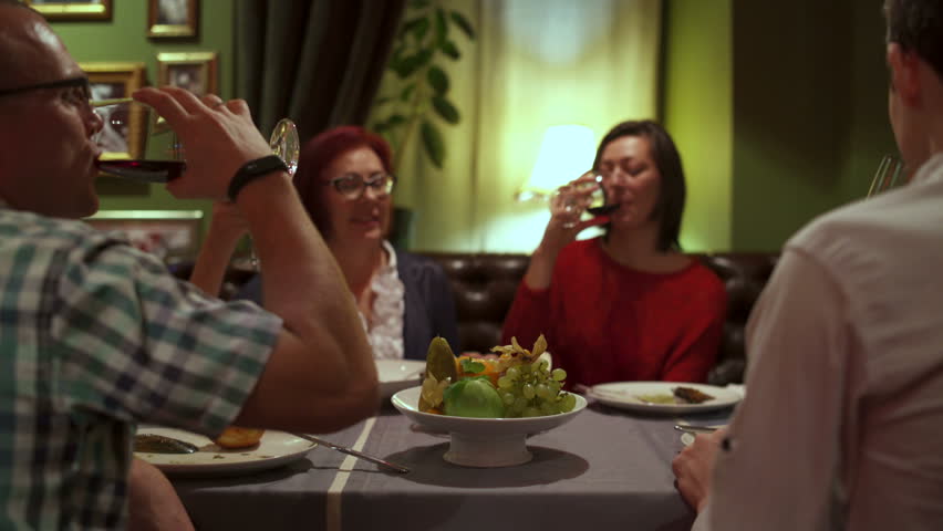 Group of friends sit at a table in the restaurant clink glasses and drink red wine | Shutterstock HD Video #1012681586