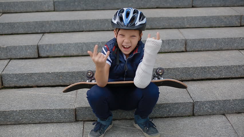 White boy with broken arm makng the rock sign sitting on the granite stairs with his skateboard.