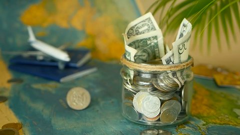 Travel budget concept. Money saved for vacation in glass jar with world map, passport and plane. Banknotes and coins for adventure. Savings for journey. Collecting money for trip. Moneybox with cash.