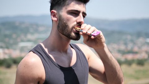 Young muscular man eating protein bar outdooron a balcony in summer
