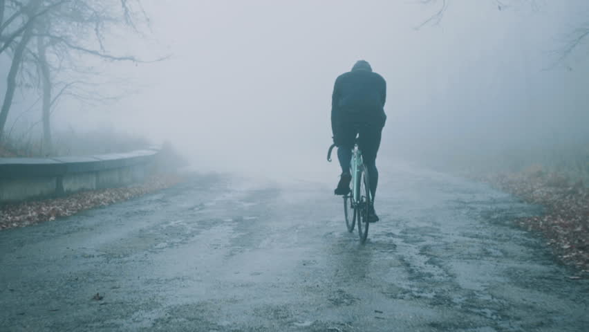 Cyclist riding a fixed bike on a small country road through foggy autumn forest