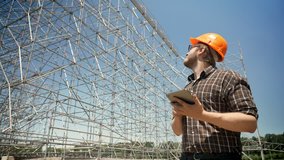 Young architect holding tablet and looking at metal installation on background, frowning and serious, planning and designing new project - Powered by Shutterstock - Get 15% off with code: PIKWIZARD15