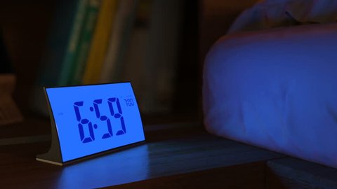 Digital alarm clock waking up at 7 AM. Close-up view. The numbers on the clock screen changes from 6:59 no 7:00 AM. Then alarm logo appears on the screen. 3D rendering animation.