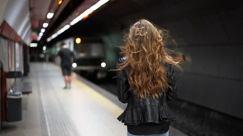 Attractive woman in an underground subway station checking her phone as a train arrives in slow motion