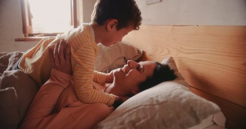 Young son relaxing and lying in bed and kissing mother in the morning