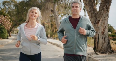 Active senior husband and wife having fun doing cardio exercise and running together outdoors