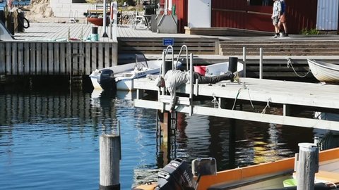 Kyrkesund, Tjorn, Sweden - May 18, 2018: Everyday life and place. Person lying on a pier while adjusting a chain hanging from the side of the pier.