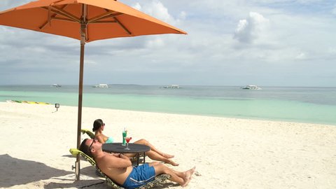 A man and a woman sunbathing on sunbeds near the sea