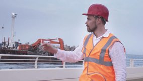 Man in a helmet, architect, engineer, manager tells about the course of repair work of the coastline with a stone stock footage video