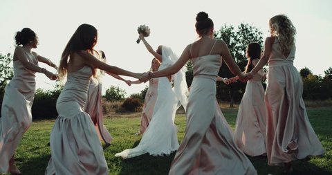 Gorgeous bride and her bridesmaid dancing amazing on the grass with amazing sunlight. red epic
