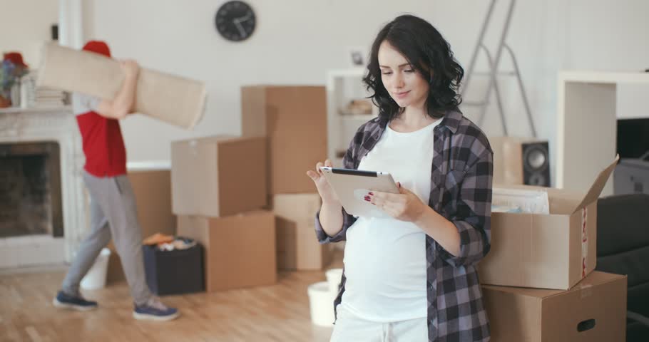 Courier brought furniture to a young pregnant woman with a smartphone in a new apartment. Concept of moving and mortgages. | Shutterstock HD Video #1012750073