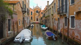 Perspective of small side canal with church in the end and moored boats in Venice, Italy