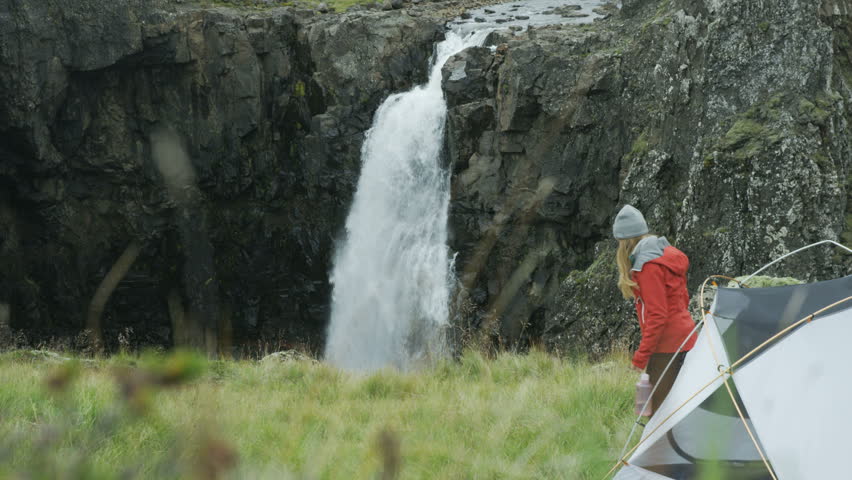 woman gets out of tent, walks towards waterfall