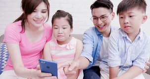 family sit on sofa and use phone happily at home