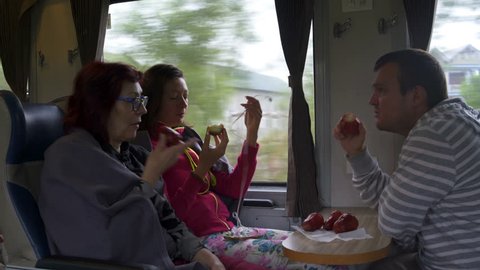 A man and women are sitting on the train, eating Malayan apples and talking