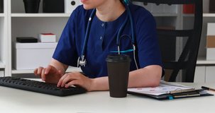 Cropped image of doctor sitting at workplace and working on computer.
