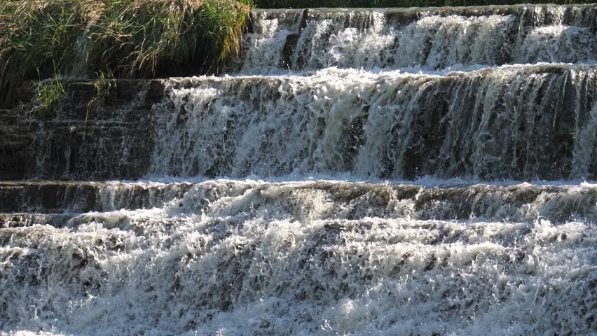 Close up slow motion view panning down the rocky stepped cliff of the beautiful Thunder Bay Waterfall as water splashes down the limestone surface into the pool below in Galena Illinois.