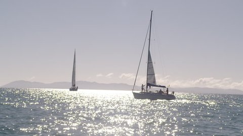 A full shot of two small boats in the middle of the ocean. The sun is shining giving a sparkling relfection to the water.