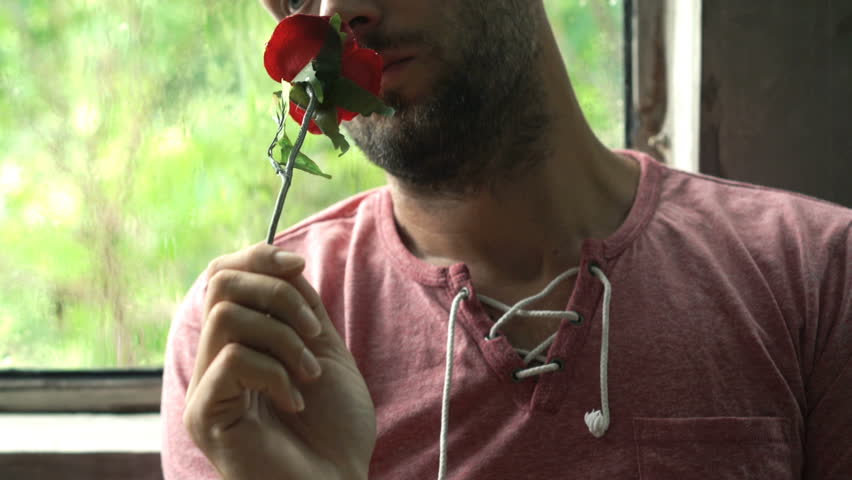 Sad, pensive man holding red rose sitting by window during rainy day 
 | Shutterstock HD Video #1012795607