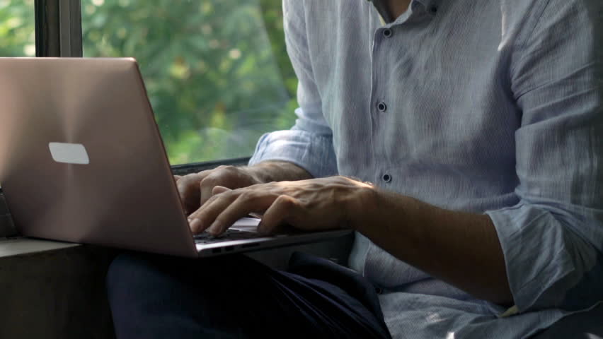 Young man using laptop sitting by window at home 
