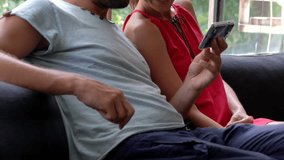 Happy couple watching movie on smartphone sitting on sofa at home
