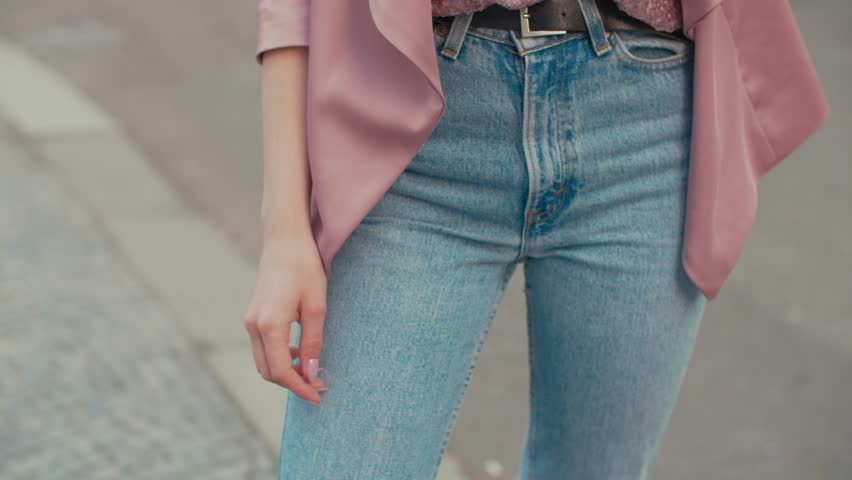 Young beautiful fashionale woman wearing high waisted jens, pink jacket, sequin shirt, wrist watch, transparent glasses posing in street