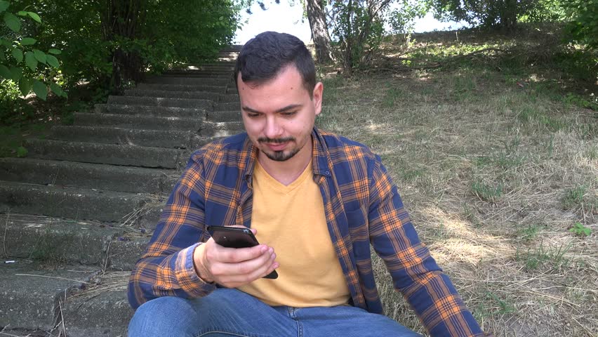 Carefree careless attractive male guy lonely in the park checking mobile phone 